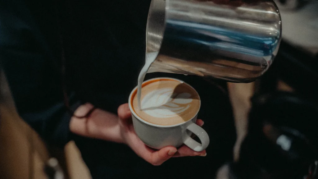 un pichet incliné avec du lait qui coule et dessine un latte art dans un coffee shop à Toulouse